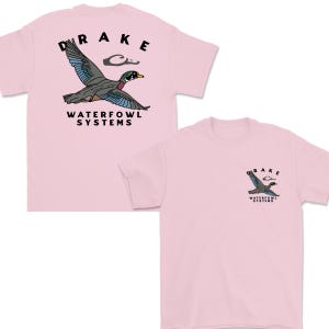 May include: Light pink t-shirts featuring a flying duck graphic with the word "DRAKE" above and "WATERFOWL SYSTEMS" below. One shirt has a large graphic on the back, and the other has a smaller graphic on the front.