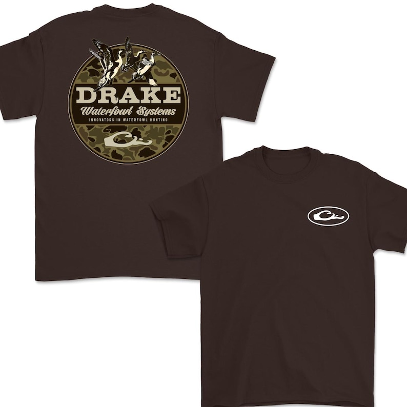 May include: Two brown t-shirts. One features a circular design with the text "DRAKE Waterfowl Systems" and a camouflage background with ducks. The other shirt has a white logo on the chest. Both shirts are short-sleeved.