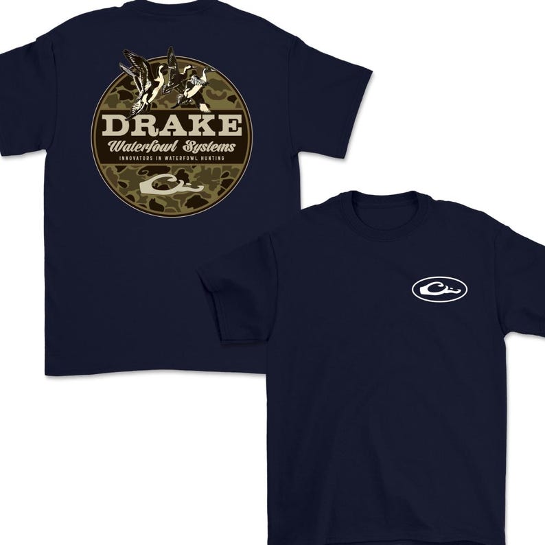 May include: Navy blue t-shirts with a crew neck. One shirt features a circular design with the text "DRAKE Waterfowl Systems" and a camouflage background. The other shirt has a white logo on the chest.