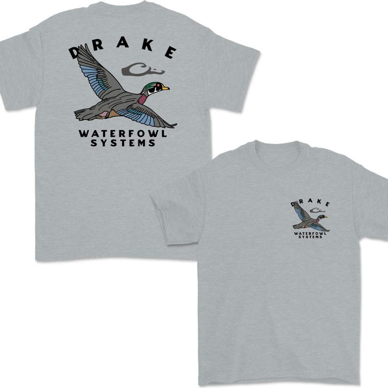 May include: Two light gray t-shirts with a duck graphic. The graphic includes a flying duck with blue, green, and red accents, the word "DRAKE" above the duck, and "WATERFOWL SYSTEMS" below. One shirt has a large graphic, the other a smaller one.