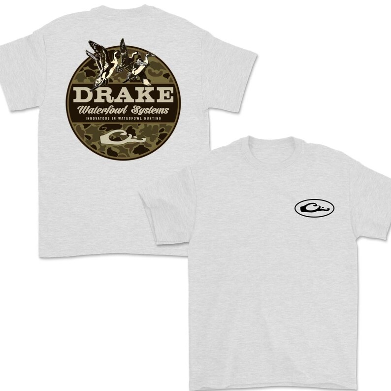May include: Light gray t-shirts with a round graphic on the back featuring the text "DRAKE Waterfowl Systems" and a camouflage pattern. The graphic includes illustrations of ducks. A smaller logo is on the front.