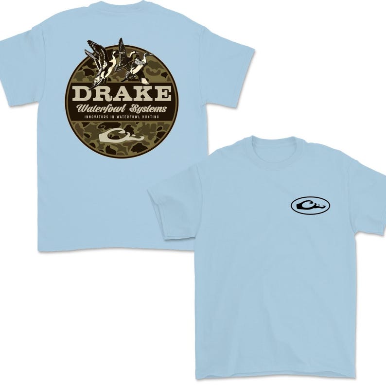May include: Light blue t-shirts with a crew neck. One shirt features a circular design with the word "DRAKE" and the text "Waterfowl Systems" with a camouflage background and duck illustrations. The other shirt has a small black oval logo.