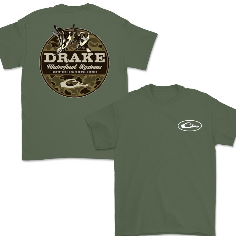 May include: Olive green t-shirts. One shirt features a circular graphic with the text "DRAKE Waterfowl Systems" and a duck illustration. The other shirt has a white oval logo on the chest. Both shirts are short-sleeved.