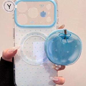May include: Clear phone case with a light blue border and apple-shaped pop socket. The case has a dotted pattern and apple and bow graphics. The pop socket is light blue with star details.