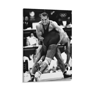 May include: Monochrome image of two wrestlers engaged in a match. One wrestler, with a focused expression, is lifting the other. Both are wearing singlets and athletic shoes, competing in a wrestling match.