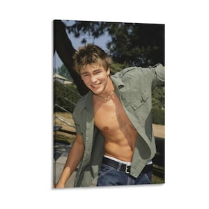 May include: A canvas print featuring a smiling person wearing a green button-down shirt, unbuttoned, over bare skin. The person is also wearing blue jeans and a necklace. The background includes trees and a staircase.