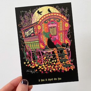 May include: A colorful, illustrated fortune teller's wagon with a woman sitting on the steps. The wagon is decorated with stars, moons, and the words "Fortune Teller". The text "I Put A Spell On You" is at the bottom of the image.
