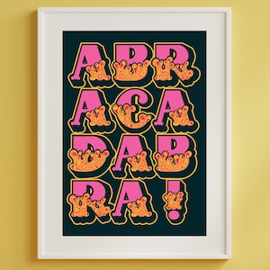 May include: A framed art print featuring the word "ABRACADABRA!" in large, stylized letters. The letters are pink with a yellow outline and orange, textured accents. The background is dark teal, and the frame is white.