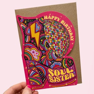 May include: A colorful birthday card with a retro design. The card features a pink boot shape with a disco ball, lightning bolt, and the words "Happy Birthday" and "Soul Sister". The background is a kraft paper color.