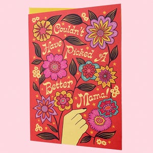 May include: A red card with a floral design and the text "Couldn't Have Picked A Better Mama!" in a retro font.
