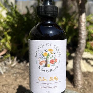 May include: A dark glass bottle with a black dropper top. The label reads "Breath of Earth Herbal Apothecary" with a floral illustration and the words "Calm Belly Herbal Tincture". The bottle contains 118 ml of liquid.