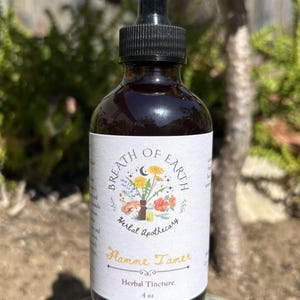 Könnte beinhalten: Eine dunkelbraune Glasflasche mit schwarzem Tropfaufsatz. Das Etikett trägt die Aufschrift "Breath of Earth Herbal Apothecary" und "Flamme Tamer Herbal Tincture". Die Flasche enthält 118 ml Flüssigkeit und steht auf einem Stein.