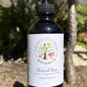 Puede incluir: Una botella de vidrio oscuro con un cuentagotas negro. La etiqueta dice "Breath of Earth Herbal Apothecary" y "Cranial Ease Herbal Tincture". La etiqueta presenta una ilustración floral. La botella contiene 118 ml de líquido.