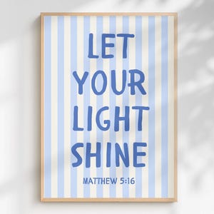 Puede incluir: Una lámina decorativa rectangular con rayas verticales de color azul claro y blanco. El texto "LET YOUR LIGHT SHINE" está impreso en una fuente azul, negrita y manuscrita, seguido del texto más pequeño "MATTHEW 5:16" en el mismo color azul.