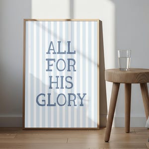 May include: A rectangular framed wall art print featuring vertical light blue and white stripes with the dark blue text ALL FOR HIS GLORY centered in a serif font. The print is displayed in a wooden frame with a clean, simple design.