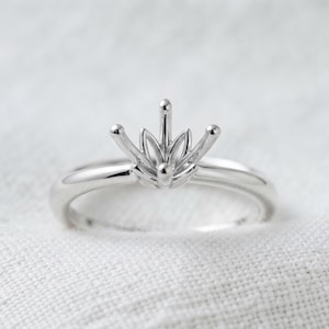 May include: A polished silver-toned ring featuring a central prong setting designed to hold a gemstone. The setting has a distinct lotus flower shape with multiple metal petals and four upright prongs extending from the base of the ring band.