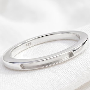 Könnte beinhalten: Ein polierter silberfarbener Ring mit einer glatten, abgerundeten Ringschiene, die auf der Vorderseite eine rechteckige, vertiefte Rinne aufweist. Die Innenseite des Rings ist deutlich mit dem Stempel 925 versehen, der das Metall angibt.