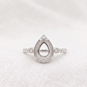 May include: A silver-toned ring featuring a pear-shaped setting with an open centre. The teardrop-shaped frame is accented with small, clear, round stones and intricate beaded metal detailing along the edges and the band of the ring.