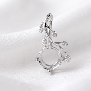 May include: A silver-toned metal pendant setting featuring a circular center mount for a gemstone. The design includes a curved branch-like stem extending upward, adorned with five small, clear, round-cut stones set into leaf-shaped metal accents.