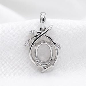 May include: A silver-toned metal pendant setting featuring an oval-shaped center mount for a gemstone. The frame is accented with three small, round, clear stones set along a branch-like design that curves around the central oval opening.