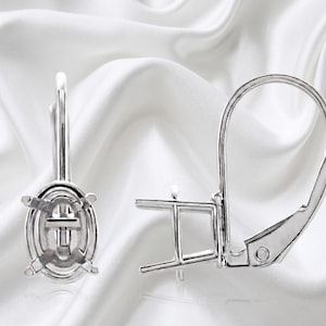 May include: A pair of silver-toned metal earring settings featuring an oval-shaped prong mounting for a gemstone. Each earring includes a secure lever-back closure mechanism, designed to hold a single stone in a vertical orientation.