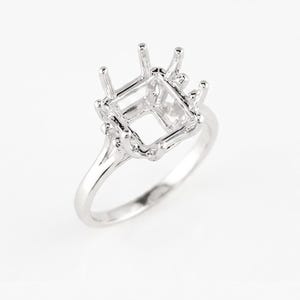 Può includere: Un castone per anello in argento con parte superiore quadrata e quattro griffe. L'anello ha una fascia delicata e un design aperto, perfetto per una pietra preziosa personalizzata. L'anello è mostrato su sfondo bianco.