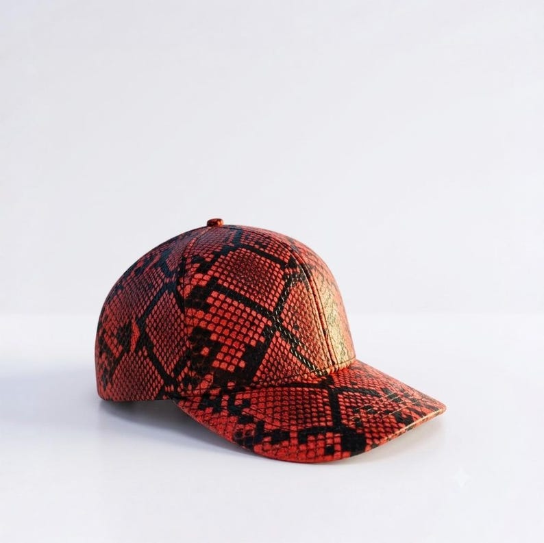 May include: A baseball cap featuring a vibrant orange and black snakeskin pattern across the entire surface. The cap has a structured six-panel crown, a curved brim, and a small button at the top center, showcasing a detailed reptilian texture.
