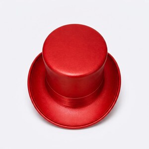 May include: A top hat in a vibrant, solid red color viewed from directly above. The hat features a flat, circular crown and a wide, circular brim. The surface has a smooth, uniform texture with a subtle sheen, showing a consistent red tone throughout.