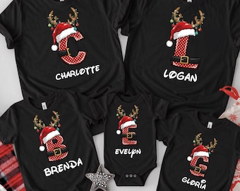 May include: Five black shirts and a baby bodysuit featuring red polka-dot letters C, L, B, E, and G. Each letter is decorated with a Santa hat, reindeer antlers, and a black belt. The names Charlotte, Logan, Brenda, Evelyn, and Gloria are printed below.