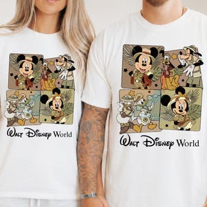 Puede incluir: Camisetas blancas con un gr&aacute;fico colorido de Mickey y Minnie Mouse, Goofy y Donald Duck con trajes de safari. El texto "Walt Disney World" est&aacute; impreso debajo del gr&aacute;fico en escritura negra.