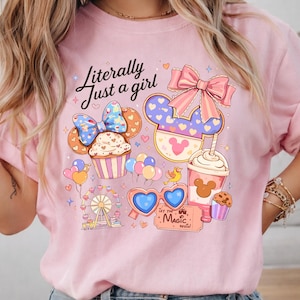 Pode incluir: Camisola rosa claro com um design gr&aacute;fico colorido. O design inclui um cupcake, orelhas do Mickey, uma bebida e uma roda gigante. O texto "Literally Just a girl" est&aacute; escrito em it&aacute;lico. O design inclui cora&ccedil;&otilde;es, la&ccedil;os e a frase "Let the Magic Begin!"