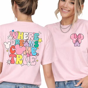 May include: Light pink t-shirts with a colorful graphic design. One shirt features the text "WHERE DREAMS COME TRUE" with Mickey Mouse-themed elements. The other shirt has a Minnie Mouse bow and castle design.