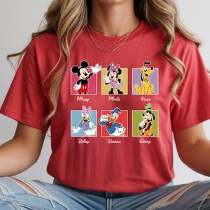 May include: Red t-shirt featuring six Disney characters: Mickey, Minnie, Pluto, Daisy, Donald, and Goofy. Each character is in a colorful square with their name below. The shirt is a solid red color.