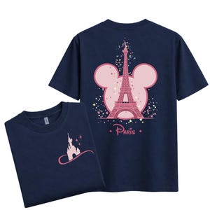 May include: Navy blue t-shirts featuring a pink Eiffel Tower design within a Mickey Mouse silhouette on the back. The front of the shirt displays a pink castle design. The word "Paris" is written below the Eiffel Tower.