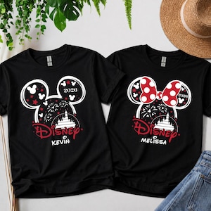 May include: Two black t-shirts with Disney designs. One has a Mickey Mouse head outline with red stars and the name "Kevin." The other features a red polka-dot bow and the name "Melissa." Both shirts include the year "2026."