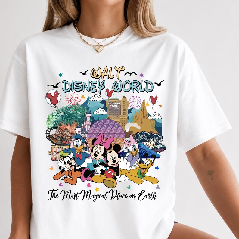 K&ouml;nnte beinhalten: Wei&szlig;es T-Shirt mit einem farbenfrohen Aufdruck von Walt Disney World-Charakteren und Wahrzeichen. Das Design zeigt Micky und Minnie Maus, Donald Duck und Pluto, mit dem Text "Walt Disney World" und "The Most Magical Place on Earth."