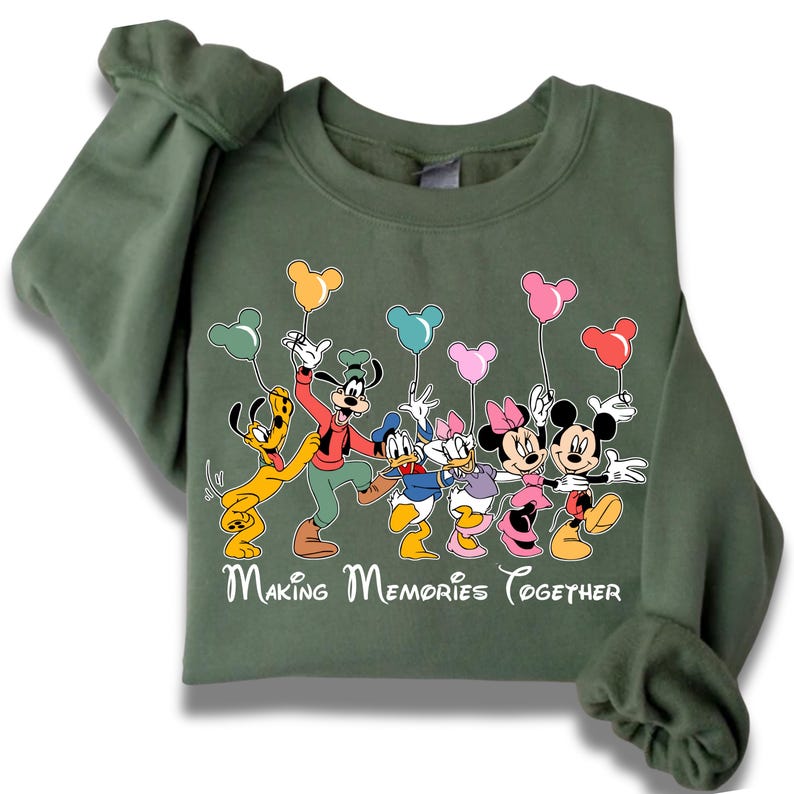 May include: Green sweatshirt featuring a graphic of Disney characters including Mickey Mouse, Minnie Mouse, Donald Duck, Daisy Duck, Goofy, and Pluto, holding balloon-shaped balloons. The text "Making Memories Together" is printed below the characters.