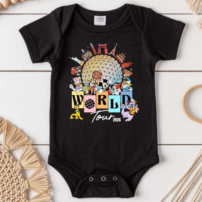 May include: Black baby bodysuit with a colourful graphic of Disney characters and landmarks. The design includes the text "WORLD Tour 2026" with Mickey Mouse, Donald Duck, and other characters. The bodysuit has short sleeves and snap closures.