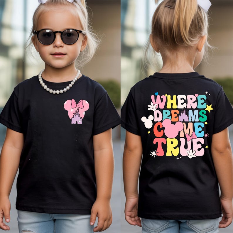 May include: Black t-shirt with a Minnie Mouse design on the front and the text "WHERE DREAMS COME TRUE" on the back. The design includes a pink bow, castle, and colourful text. The shirt is worn by a child.