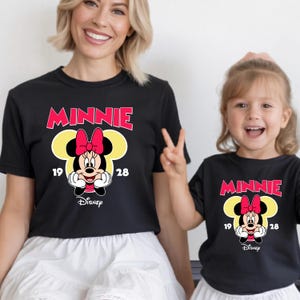 May include: Black t-shirts featuring a Minnie Mouse design. The design includes the word "MINNIE" in red, a yellow silhouette of Minnie's head, and a cartoon image of Minnie Mouse. The Disney logo is at the bottom.