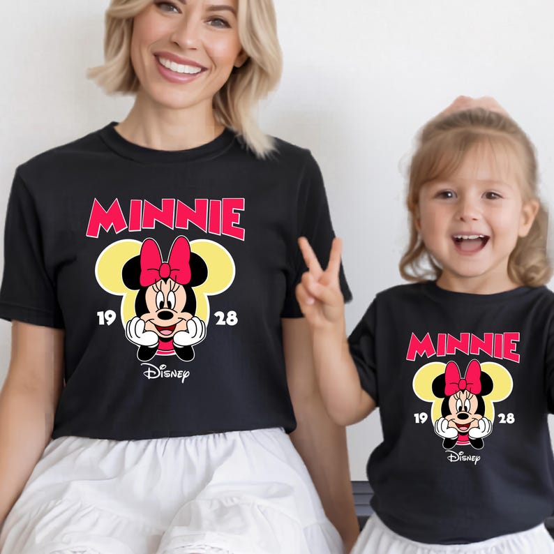 May include: Black t-shirts featuring a Minnie Mouse design. The design includes the word "MINNIE" in red, a yellow silhouette of Minnie's head, and a cartoon image of Minnie Mouse. The Disney logo is at the bottom.