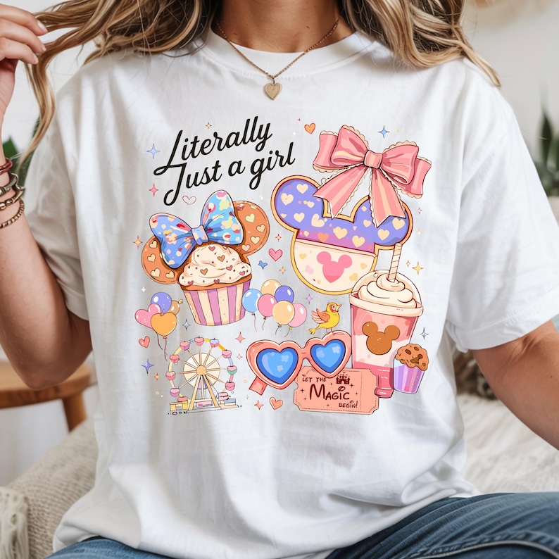 Pode incluir: Camiseta branca com o texto "Literally Just a girl" e um gr&aacute;fico colorido com um cupcake, orelhas do Mickey, uma roda gigante, &oacute;culos de sol em forma de cora&ccedil;&atilde;o e uma x&iacute;cara de caf&eacute;. O gr&aacute;fico inclui detalhes em rosa, azul e amarelo.