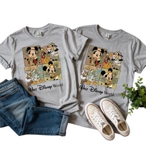 Puede incluir: Dos camisetas grises con un gr&aacute;fico colorido con Mickey Mouse, el Pato Donald, Goofy y otros personajes de Disney con trajes de safari. El texto "Walt Disney World" est&aacute; impreso debajo. Tambi&eacute;n hay unos vaqueros azules y zapatillas blancas.