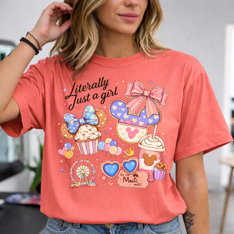 Pode incluir: Camiseta coral com um gr&aacute;fico l&uacute;dico. Apresenta um cupcake, orelhas do Mickey Mouse, uma roda gigante, &oacute;culos de sol em forma de cora&ccedil;&atilde;o e o texto "Literally Just a girl". O design inclui la&ccedil;os, bal&otilde;es e uma x&iacute;cara de caf&eacute;.