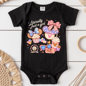 Pode incluir: Body de beb&eacute; preto com um design gr&aacute;fico colorido. O design inclui um cupcake, uma roda gigante, &oacute;culos de sol em forma de cora&ccedil;&atilde;o e uma bebida com uma cabe&ccedil;a do Mickey Mouse. O texto diz "Literally Just a girl" e "Let the Magic Begin".