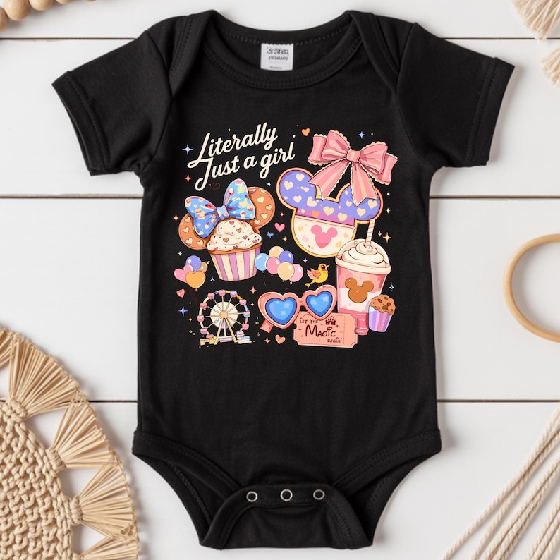 Pode incluir: Body de beb&eacute; preto com um design gr&aacute;fico colorido. O design inclui um cupcake, uma roda gigante, &oacute;culos de sol em forma de cora&ccedil;&atilde;o e uma bebida com uma cabe&ccedil;a do Mickey Mouse. O texto diz "Literally Just a girl" e "Let the Magic Begin".