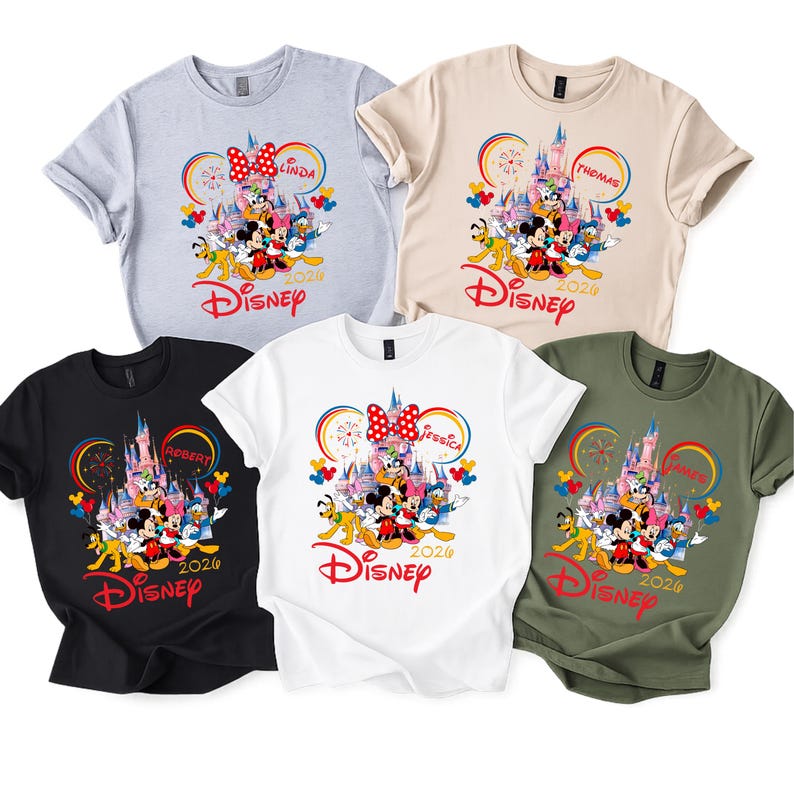 Op de afbeelding: Vijf T-shirts met korte mouwen in verschillende kleuren: lichtgrijs, beige, zwart, wit en olijfgroen. Elk shirt heeft een Disney-afbeelding met Mickey en Minnie Mouse, een kasteel en het woord "Disney" in het rood. De shirts hebben ook namen en het jaar 2024.