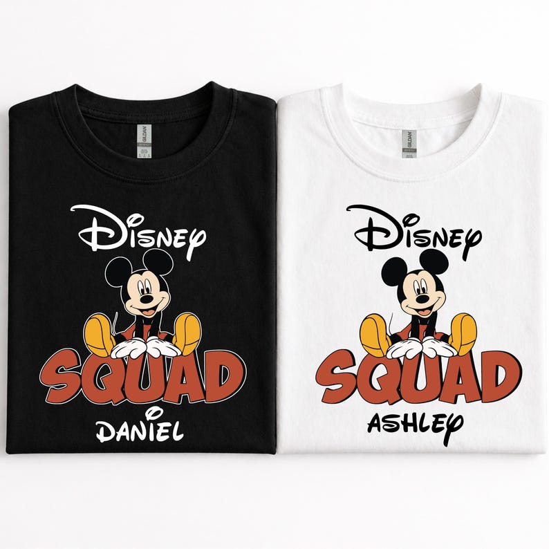 Op de afbeelding: Twee T-shirts, &eacute;&eacute;n zwart en &eacute;&eacute;n wit, met een Mickey Mouse-afbeelding. De shirts tonen het woord "Disney" boven het personage en "SQUAD" in rode letters. De naam "DANIEL" staat op het zwarte shirt en "ASHLEY" op het witte.