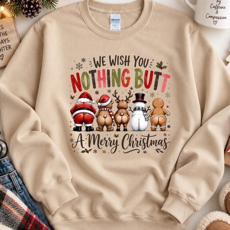 May include: A beige crewneck sweatshirt featuring a graphic of Santa, a bear, a reindeer, a snowman, and a gingerbread person facing away. The text reads "WE WISH YOU NOTHING BUTT A MERRY CHRISTMAS" in red, green, and black lettering with snowflakes.