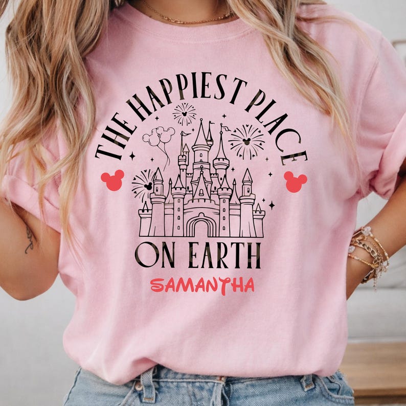 May include: A light pink sweatshirt with the text "THE HAPPIEST PLACE ON EARTH" in black, with a castle graphic and red Mickey Mouse head icons. The name "SAMANTHA" is printed in red below the text.